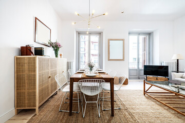 This room with a wooden dining table with white metal chairs and a mesh sideboard and a natural fiber rug