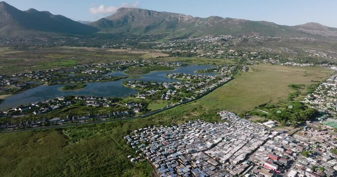 Inequality.Poverty.Aerial fly over view of the Masiphumelele informal settlement squatter camp right next to middle class suburban housing Lake Michelle,Cape Town, South Africa