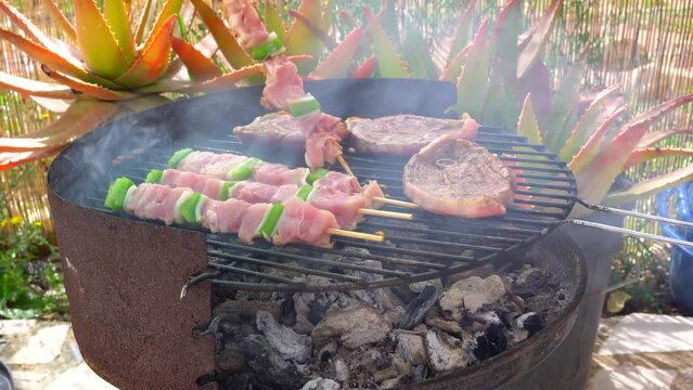 Barbacoa con mano de hombre de 4 dedos volteando la carne y los pinchos