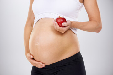 Healthy diet for the baby. Cropped image of a pregnant woman holding an apple and touching her...