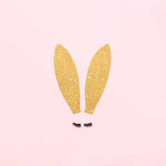 Easter bunny gold ears with lashes on a pastel pink background. Minimal Easter surreal concept. Pink aesthetic cosmetic layout.