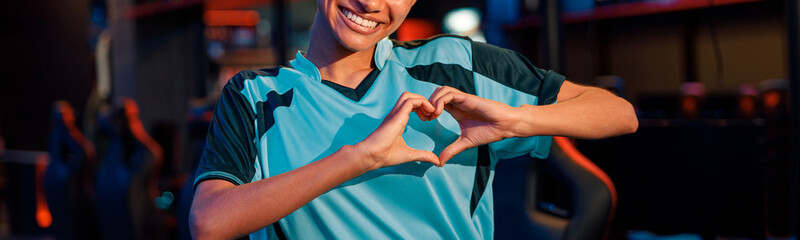 Young African woman esports gamer in blue t-shirt showing heart sign by hands with happy facial...