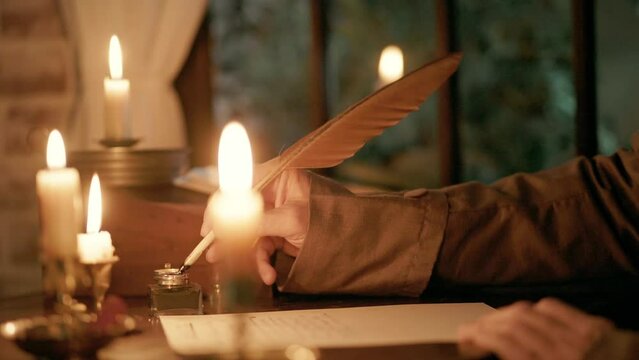 An 18th century type scene lit by multiple candles of a man sitting at his desk with inkwell and quill pen writing a letter.