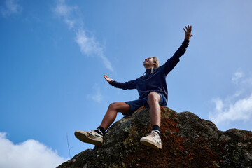 A bottom view of young man sitting on a rock with open arms