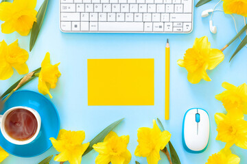 Woman's modern workspace. Keyboard, glasses and office supplies on blue table. Bouquet of delicate beautiful yellow daffodils and cup of coffee for holiday.