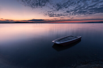 Surreal long exposure view of shore of Trasimeno lake Umbria, Italy with a little boat and perfectly still water - 492450420