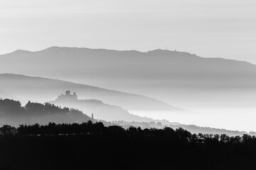 Mist and fog between valley and layers of mountains and hills in Umbria Italy with Assisi silhouette at the distance