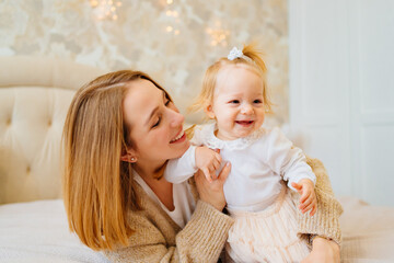 Cute mom and baby daughter lie down, play and hug in bed. games with children. 