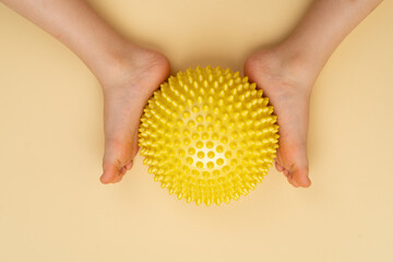 yellow needle balancing ball for massage and physiotherapy on a beige background with the image of a child's foot, the concept of prevention and treatment of hallux valgus