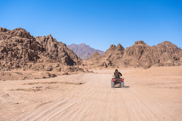 Fototapeta na wymiar Mountains landscape and person on motorbike. Quadricycle safari park in Egypt sand desert. Sharm el Sheikh, Sinai peninsula. Extreme travel on all-terrain vehicle.