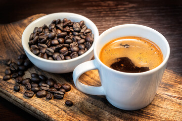 Close-up of hot black coffee in white coffee cup and roasted coffee beans in white bowl on wooden background