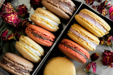 Multicolored macaroons in boxes with rose buds. Top view, selective focus natural light
