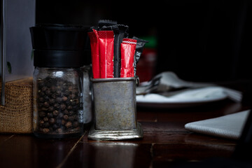Rustic metal sugar sachet and sweetner container. Restaurant table with black pepper