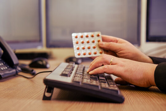 A businessman man with pills in his hands is working on a computer keyboard at an office desk, close-up