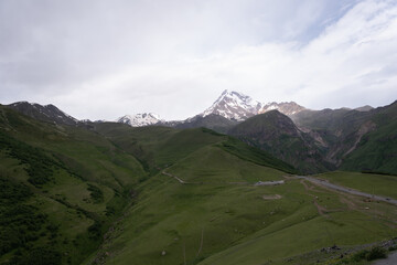 the Kazbegi mountain ranges in Georgia are green and have a clear sky above them.