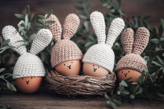 Four Easter eggs in crochet hats with rabbit ears in a nest on a wooden table. Soft focus.