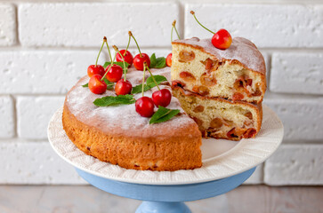 Sliced fluffy chiffon cake with fresh sweet cherry on cake plate. Light background, selective focus.