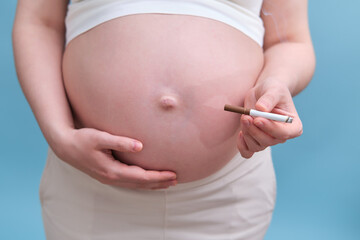 Pregnant woman with a cigarette in her hand, blue background in the studio