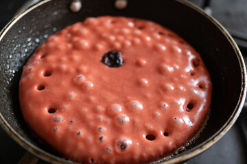 detalle de hot cake crudo sabor y color fresa en el sartén con burbujas de calor y arándonos