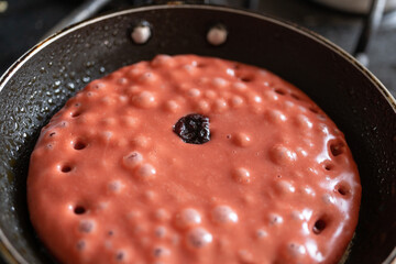 detalle de hot cake crudo sabor y color fresa en el sartén con burbujas de calor y arándonos