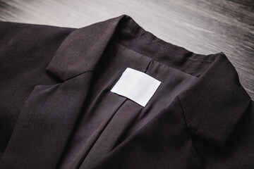 Blank clothing tag on the texture of a black blazer. Label with empty space for text