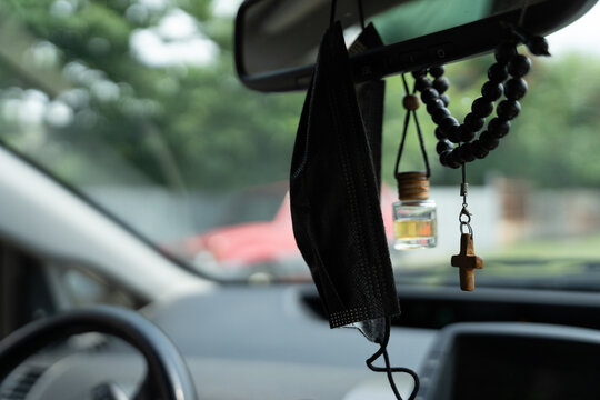 there is a black face mask and a perfume bottle next to the car mirror, next to which is a small wooden cross