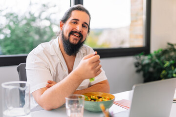 portrait of young man with beard while eating salad, smiling