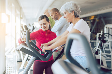 Fitness coach in gym helping senior people during cardio bike training
