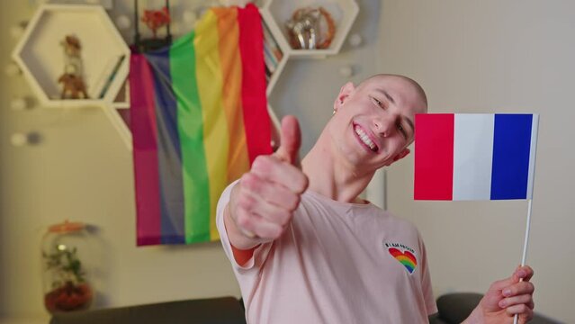 Queer caucasian happy gay man living in France, waving his French flag, and showing thumbs up to the camera. High quality 4k footage