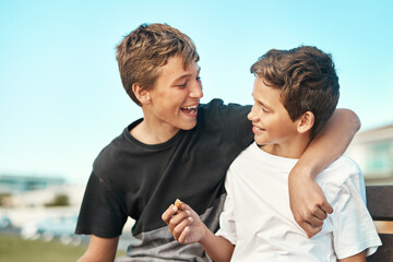 Hey, want to hear a joke. Shot of two happy brothers sitting on a bench by the beach together. - Powered by Adobe