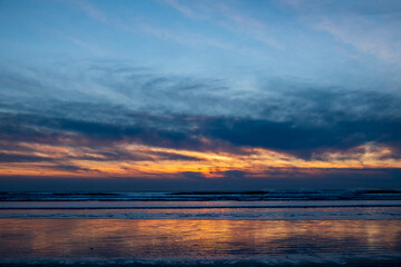 Naklejka na ściany i meble A beach with reflective sand at sunset, clouds streaking across the sky