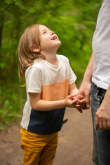 Dad and daughter walk in the forest in summer, the girl holds dad's hand