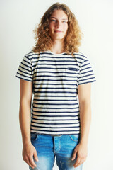 Unique and stylish. Young man with curly long hair standing by himself.