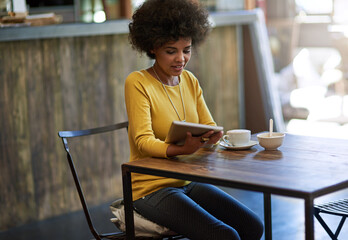 Catching up on some work. Shot of a young woman using a digital tablet in a cafe.