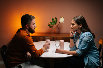 Loving young couple enjoying talking, having fun together celebrating Valentines day dining during romantic dinner date, sitting together at table with candles in cozy dark living room.