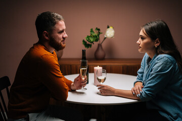 Side view of happy romantic young couple enjoying talking and sitting together at dinner table with candles in dark room. Love man and woman celebrating anniversary, Valentines day at home.