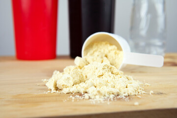 Whey protein powder in scoop with vitamins and plastic shaker on wooden background.

