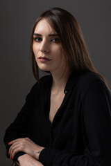 Naklejka premium Portrait of a young brunette with long hair in the studio. Dramatic photo in dark colors.