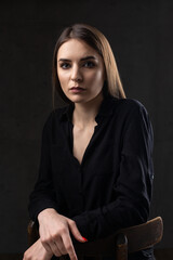 Portrait of a young brunette with long hair in the studio. Dramatic photo in dark colors.