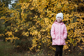 Little caucasian girl in pink coat against yellow bush autumn time