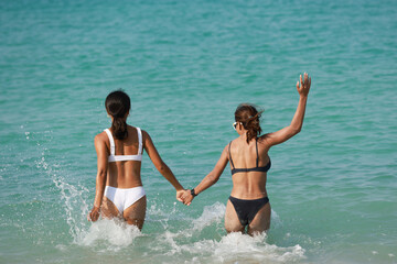 Couple Tanned women wearing bikini hand to hand walk to the sea, LGBT and summer vacation concept , Young sexy woman playing on tropical beach