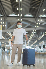 Young male wearing face mask with luggage walking in airport, protection Coronavirus disease...