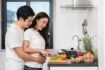 couple cutting vegetables for preparing healthy food in the kitchen at home. man is hugging woman