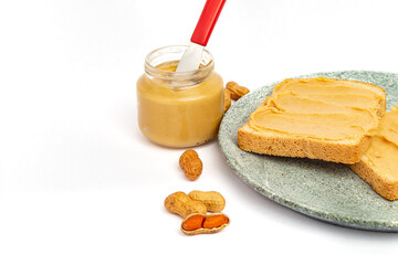 Bread with peanut butter and glass with peanut butter and knife on a white background