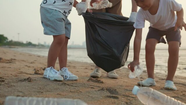 Volunteer happy family picking plastic bottle into trash plastic bag black for cleaning beach, Mother and his children clean up garbage at sunset, Ecology and World Environment Day, Save earth concept