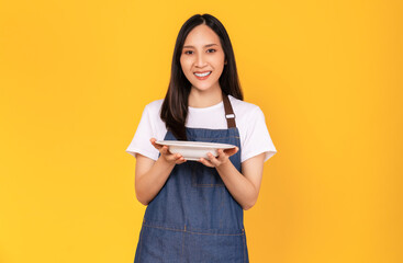 Beautiful Asian women wear apron with holding white dishes on yellow background.