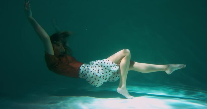 Atmospheric shot of young beautiful elegant dancer woman doing modern dance moves back flipping under water slow motion.