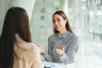 Mixed race woman worker talk explaining issue to female colleague sit together at workplace, diverse coworkers speak discuss business project sharing ideas near computer in office