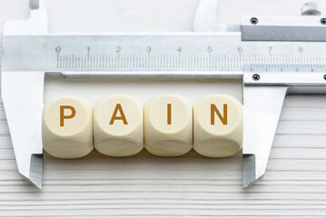 Pain rating scales, clinical concept : Vernier caliper measures wood cubes with the word PAIN,...