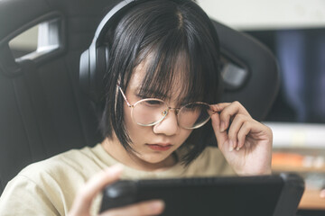 Nerd style young adult asian gamer woman wear eyeglasses and headphone play a online game